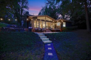 A modern house with a covered patio, outdoor seating, and a staircase leading to the entrance. - Relaxing Badin Lake Waterfront l Private Pier,Hot Tub,Pool Table-Dock Your Boat! (New London)