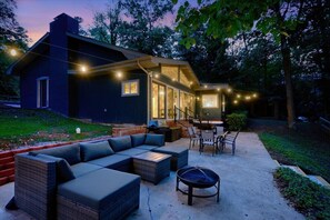 A modern outdoor living area with a built-in sofa, a dining table, and a fire pit. - Relaxing Badin Lake Waterfront l Private Pier,Hot Tub,Pool Table-Dock Your Boat! (New London)