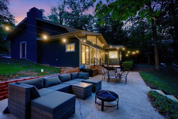 A modern outdoor living area with a built-in sofa, a dining table, and a fire pit. - Relaxing Badin Lake Waterfront l Private Pier,Hot Tub,Pool Table-Dock Your Boat! (New London)