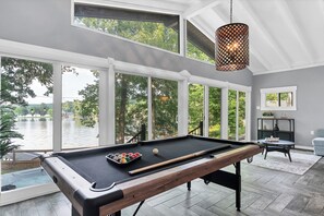 A pool table with a view of a lake, large windows, and a hanging light fixture. - Relaxing Badin Lake Waterfront l Private Pier,Hot Tub,Pool Table-Dock Your Boat! (New London)