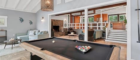 A pool table in a room with a fireplace, a sofa, and a dining area.