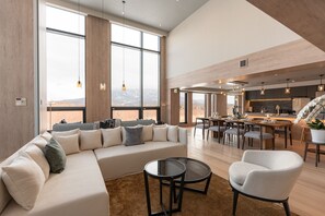 A spacious living area with a large sectional sofa, a round coffee table, and a dining table set for six. - The 1898 Niseko (Kutchan)