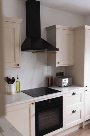 A kitchen with a black range hood, a built-in oven, a toaster, and a marble backsplash.