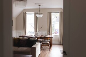 A dining area with a table set for four, a chandelier, and a view through the window. - Luxury 3-Bed Apartment in the Heart of Ambleside (Ambleside)