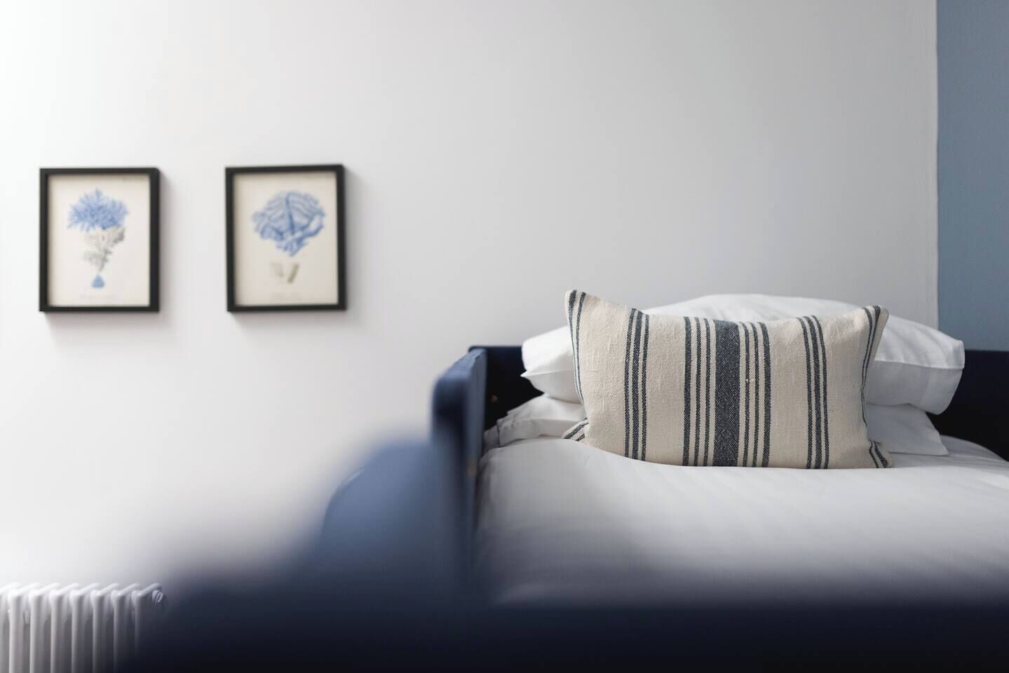 A neatly made bed with striped pillows, a dark headboard, and two framed artworks on the wall.