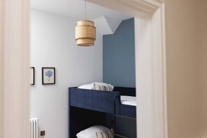 A bunk bed room with a hanging light fixture, framed artwork on the wall, and a radiator.