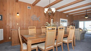 A wooden dining area with a chandelier, a large window, and a view of the outdoors. - Shore to Please: Oceanfront, Pool, Classic Beach Charm (Murrells Inlet)
