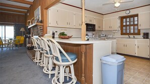 A kitchen with a bar area, wooden cabinets, a microwave, and a trash bin. - Shore to Please: Oceanfront, Pool, Classic Beach Charm (Murrells Inlet)