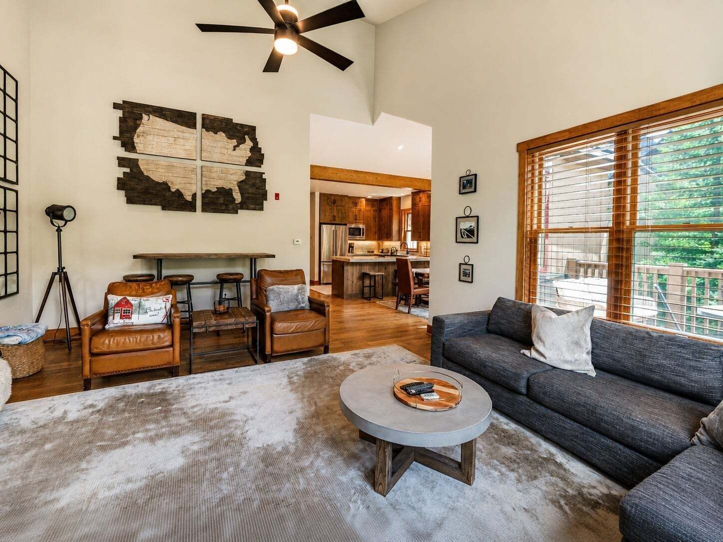 A spacious living area with a sofa, a coffee table, and a dining table. There is a kitchen in the background with wooden cabinets.