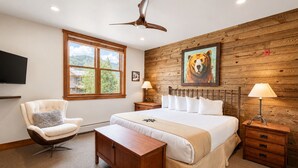Un dormitorio con una cama grande, una silla, un escritorio, un televisor y una pared de madera con un cuadro de un tigre.