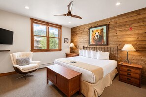 Ein Schlafzimmer mit einem großen Bett, einem Sessel, einem Schreibtisch, einem Fernseher und einer Holzwand mit einem Tigerbild.