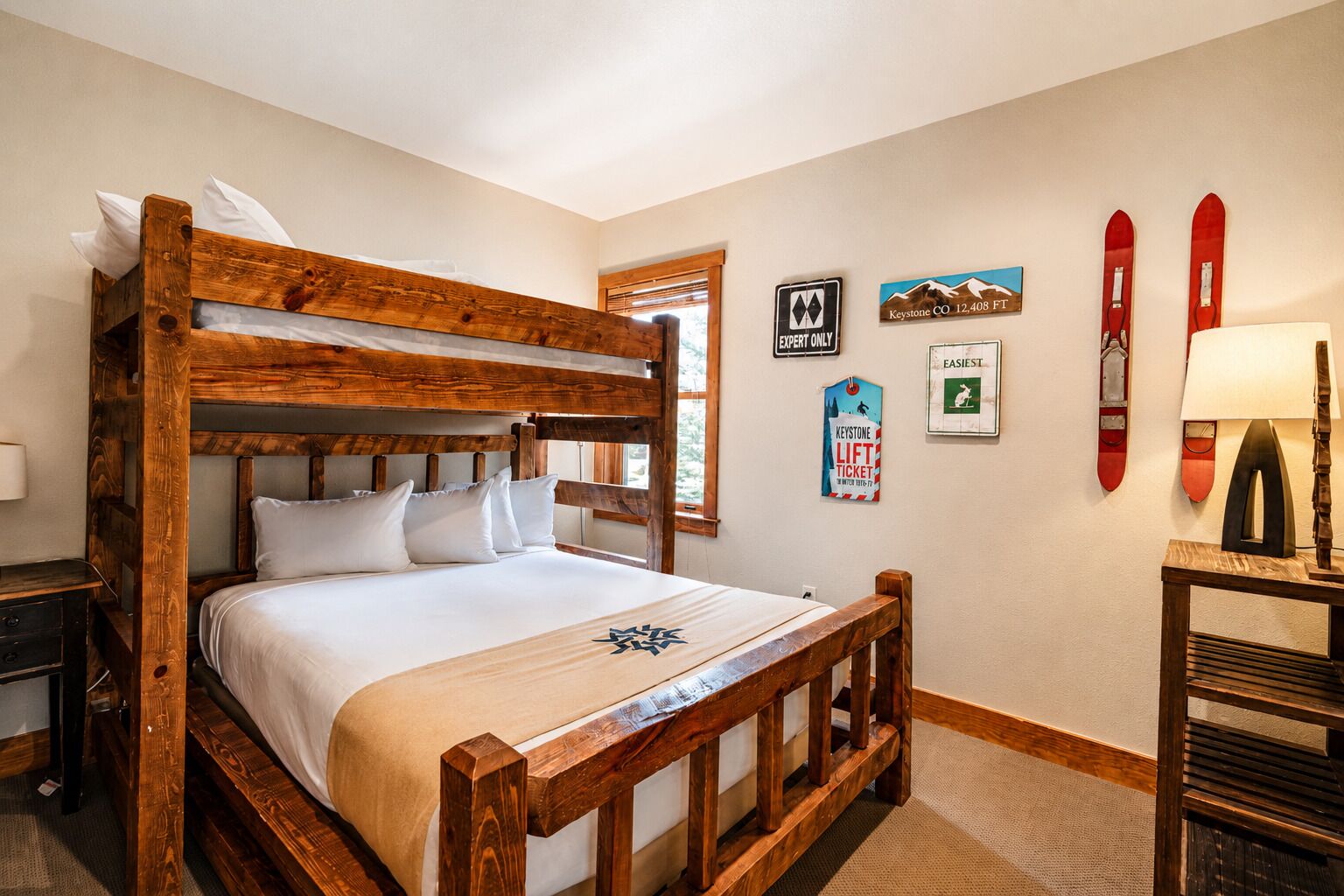 A wooden bunk bed with white bedding, a nightstand, a lamp, and ski-related decor on the walls.