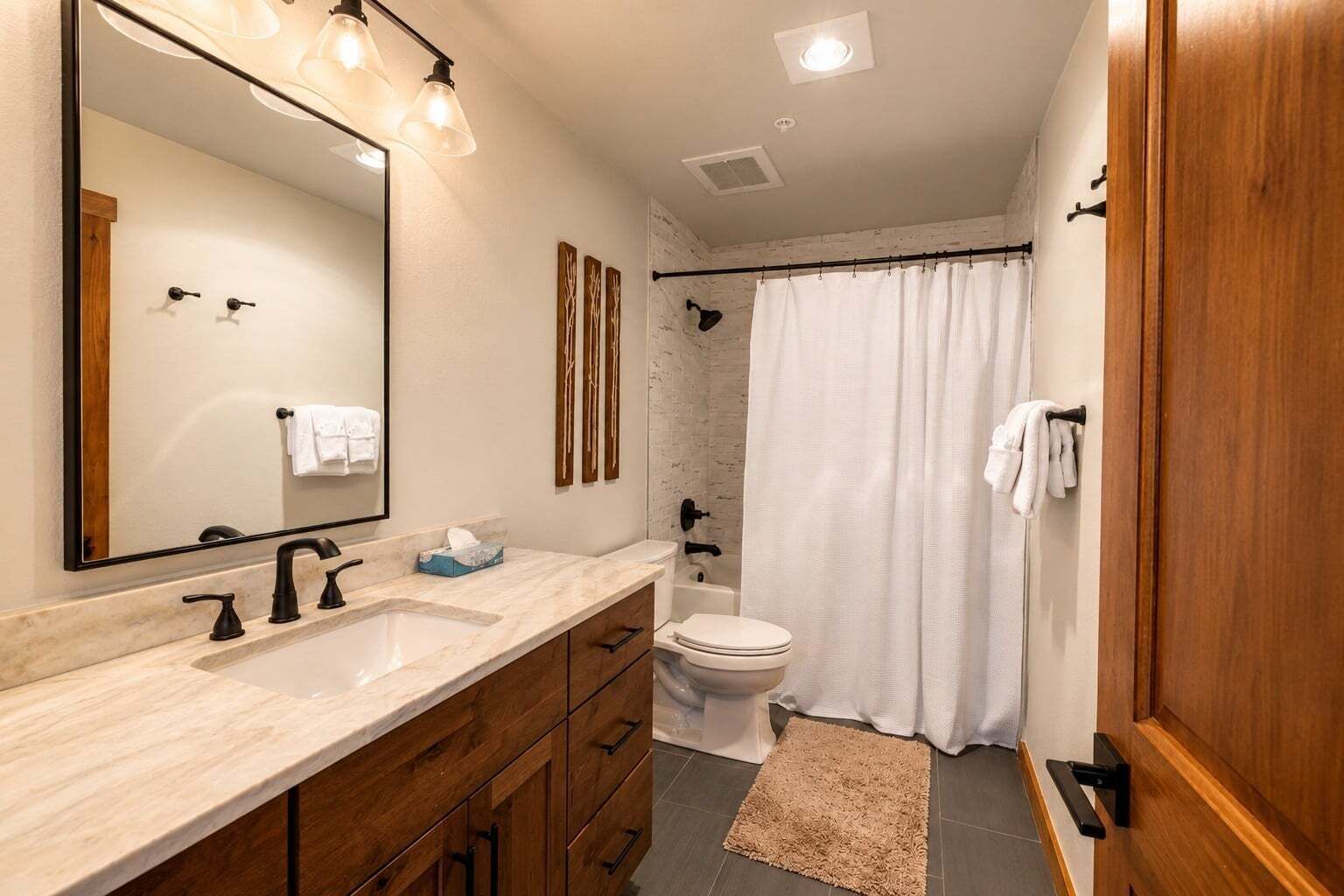 Une salle de bain avec un grand miroir, deux lavabos, des toilettes et un rideau de douche.