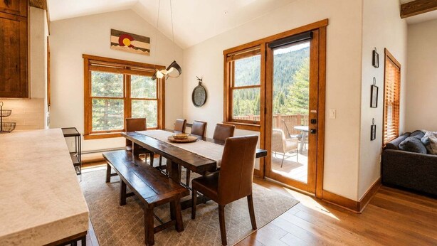 Un comedor con una mesa y sillas de madera, ventanas amplias y vistas al exterior.