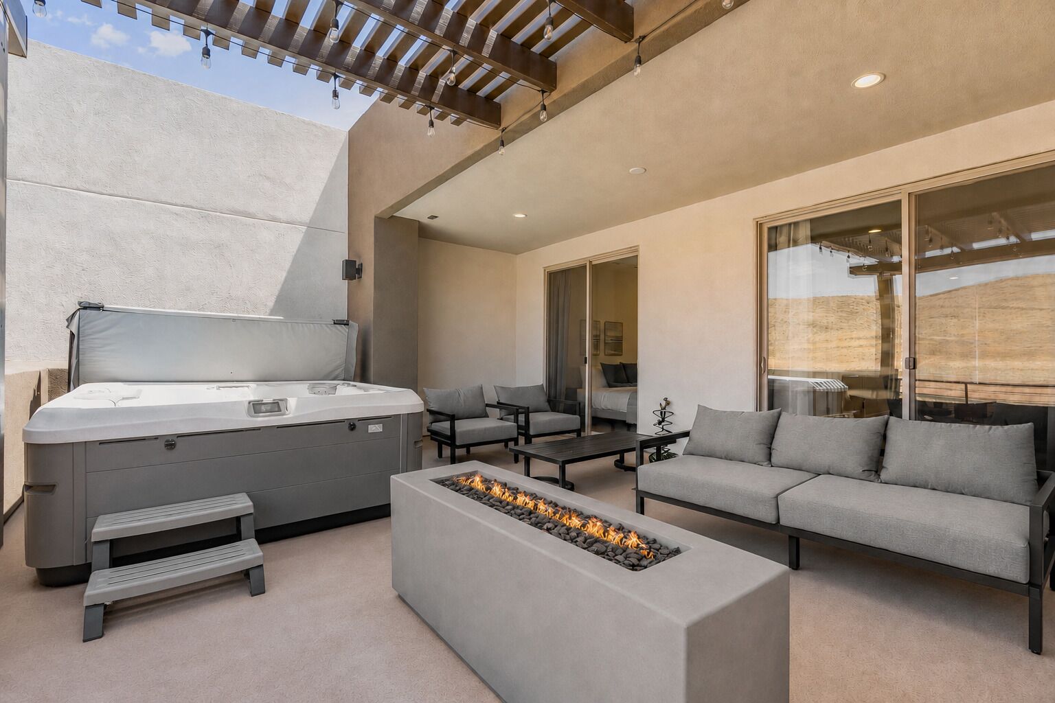 A modern outdoor patio with a hot tub, seating area, and a fire feature.