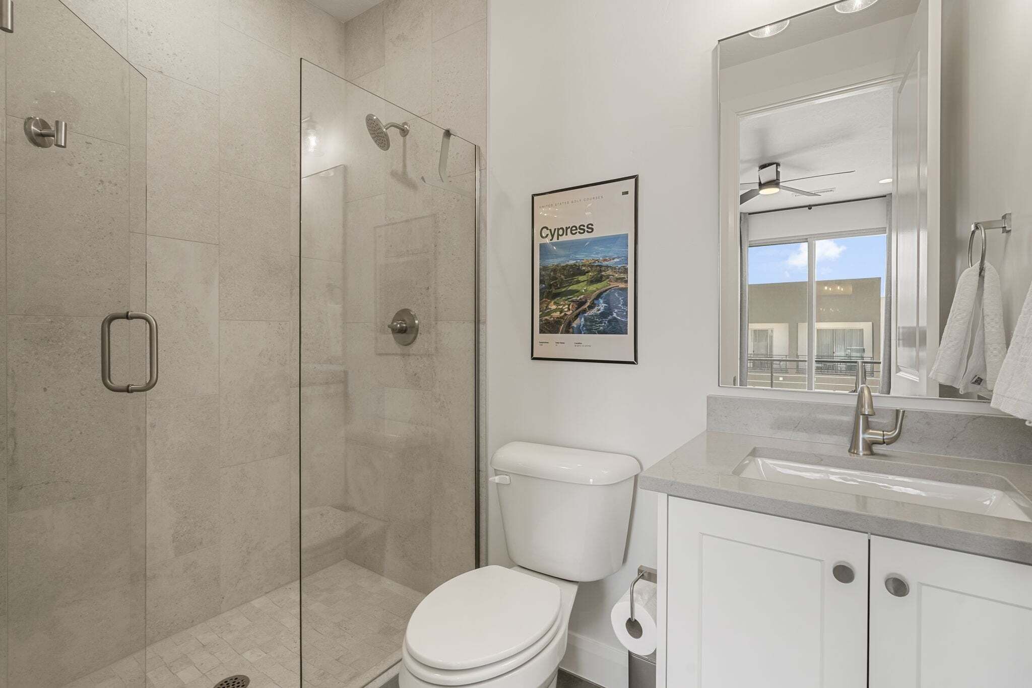 Un baño moderno con ducha de vidrio, inodoro, lavamanos y un cuadro enmarco de Chipre.