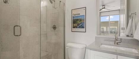 Un baño moderno con ducha de vidrio, inodoro, lavamanos y un cuadro enmarco de Chipre.