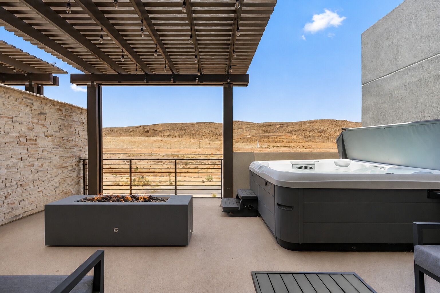 An outdoor patio with a fire pit, a hot tub, and a seating area, overlooking a desert landscape.