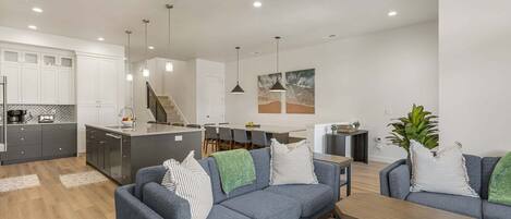 Una cocina moderna con armarios blancos, un comedor con mesa y sillas, y una sala de estar con sofá y mesa de centro.