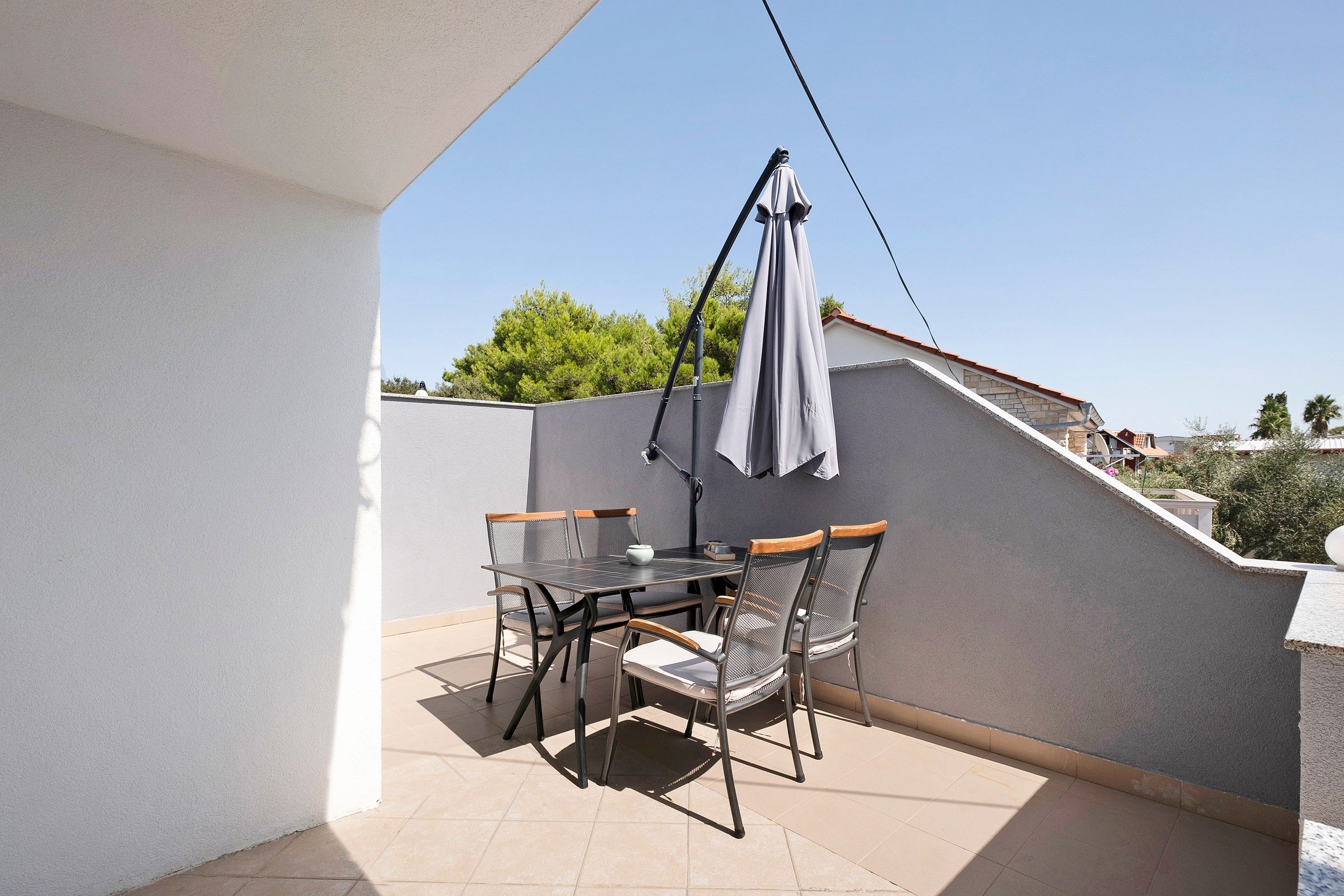 A balcony with a table and chairs, a hanging umbrella, and a view of the surrounding area.