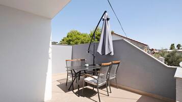 A balcony with a table and chairs, a hanging umbrella, and a view of the surrounding area.