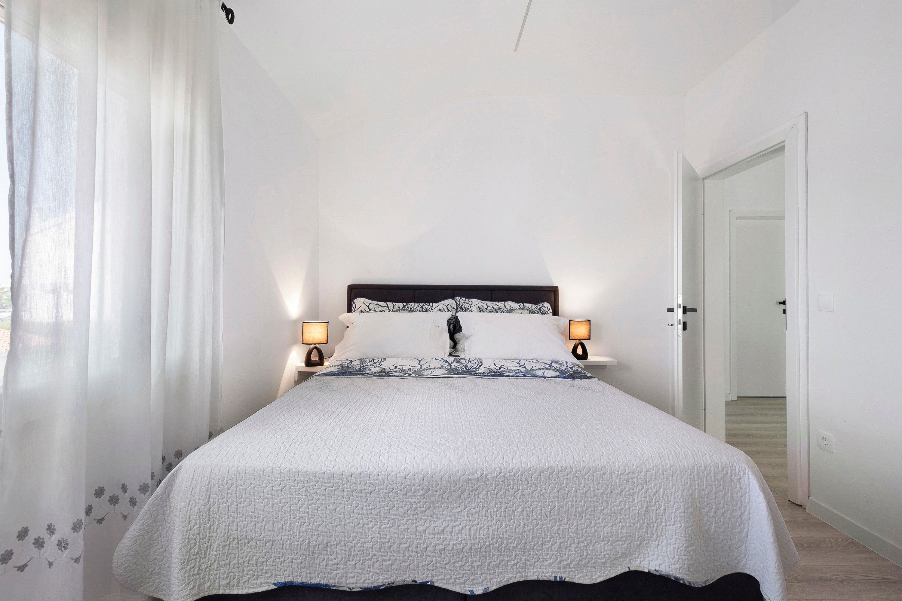 Een slaapkamer met een bed, twee bedlampen, een deur en een raam met gordijnen.