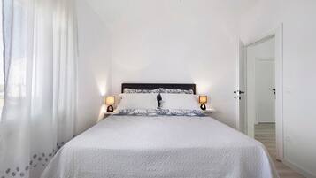 Een slaapkamer met een bed, twee bedlampen, een deur en een raam met gordijnen.