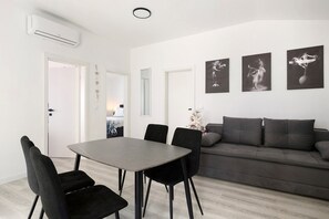 A modern living room with a grey sofa, black chairs, a dining table, and three black-and-white framed artworks on the wall.