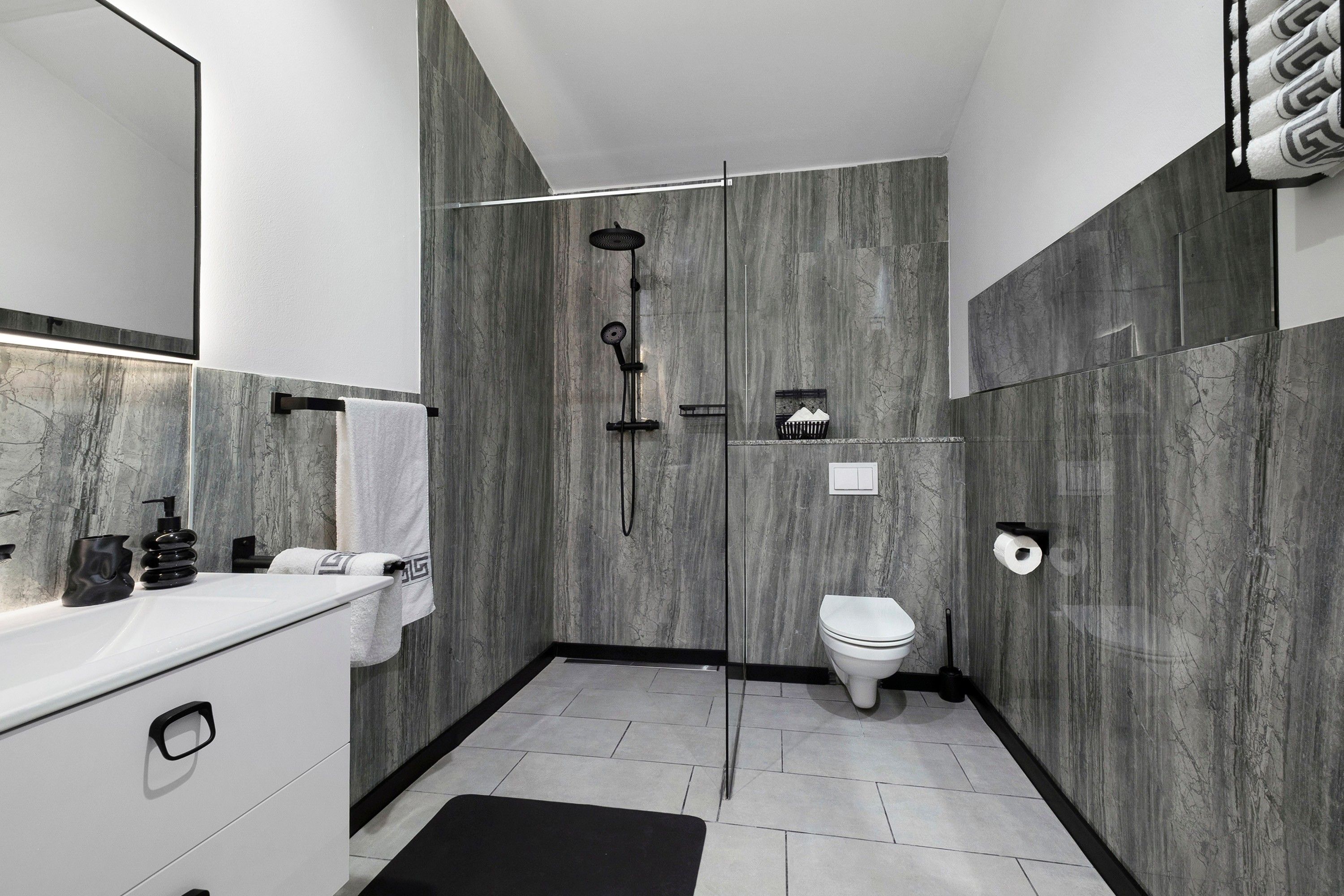 Een moderne badkamer met een marmeren wand, een witte wastafel, een zwarte handdoek en een douchegedeelte.