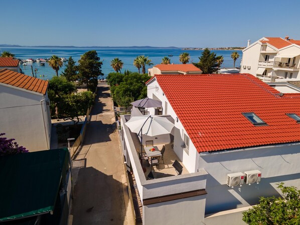 A coastal building with a red roof, a balcony with outdoor furniture, and a view of the sea.