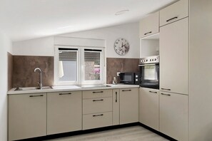 A compact kitchen with a sink, a clock, a microwave, and cabinets.