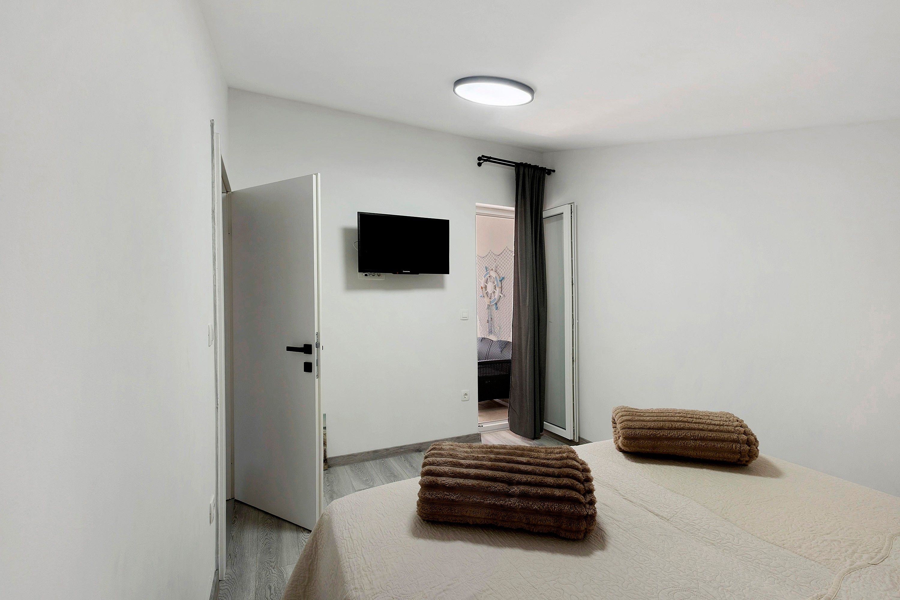 Ein Hotelzimmer mit Bett, Flachbildfernseher an der Wand, einer Tür zu einem Balkon und einem mit Vorhängen versehenen Fenster.