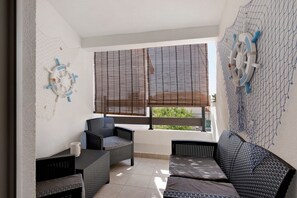 A balcony with wicker furniture, a ship's wheel decoration, and a view of greenery through the window blinds. - Modern Beach Apartment on Vir, 30m from the Beach, Sea View, Up to 4 Guests (Vir)