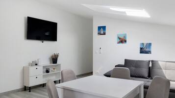 A modern room with a flat-screen TV, a white table, a grey sofa, and a small white cabinet.