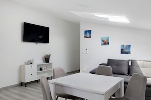 A modern room with a flat-screen TV, a white table, a grey sofa, and a small white cabinet. - Modern Beach Apartment on Vir, 30m from the Beach, Sea View, Up to 4 Guests (Vir)