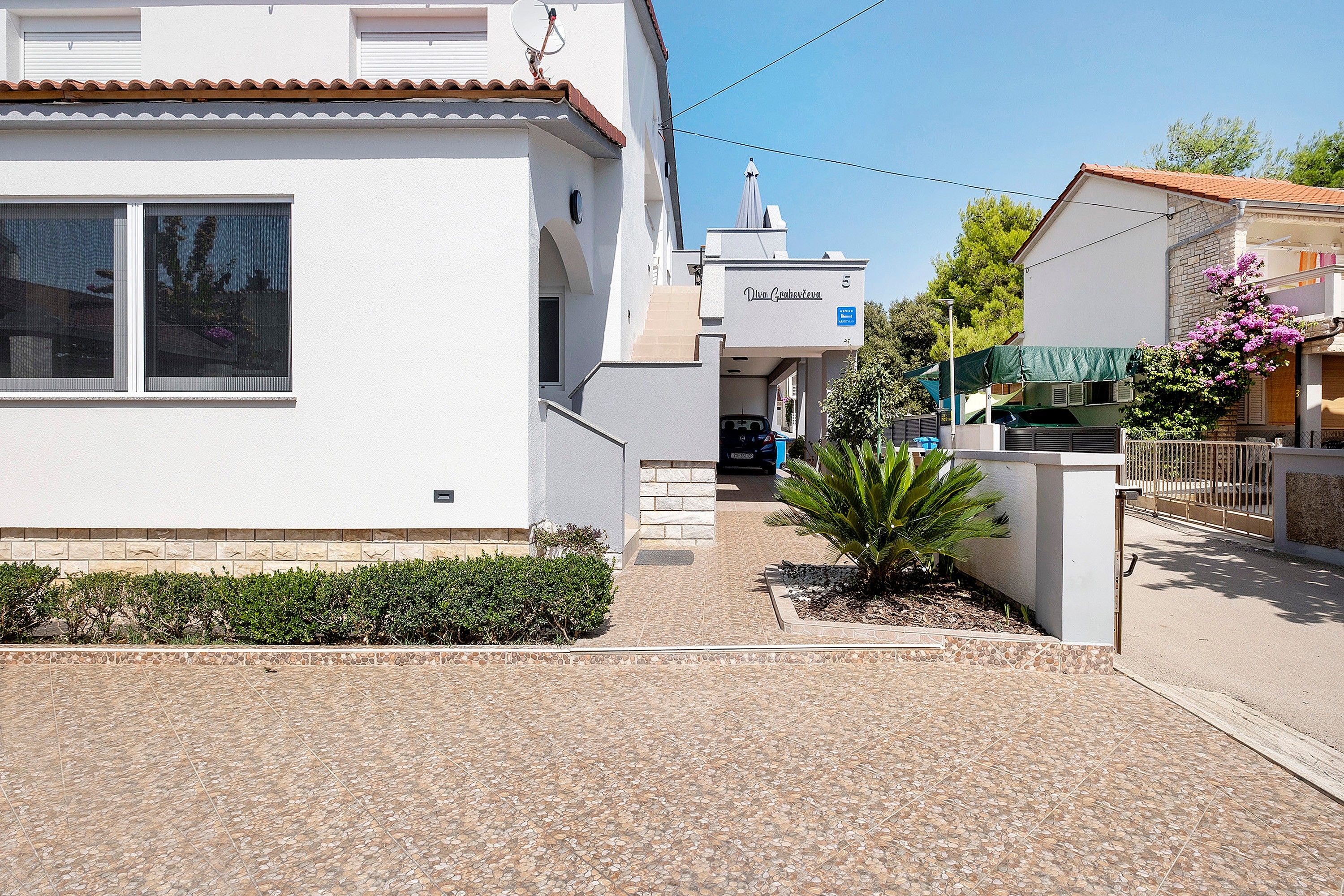 A residential building with a tiled entrance, a small garden with a palm tree, and a visible satellite dish.