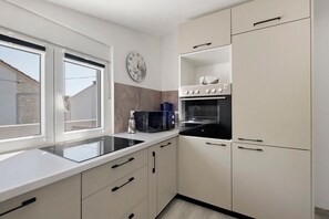 A modern kitchen with a built-in oven, microwave, and a window with blinds. - Modern Beach Apartment on Vir, 30m from the Beach, Sea View, Up to 4 Guests (Vir)