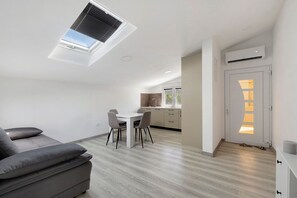 A modern living space with a dining area, a sofa, and a kitchen in the background.