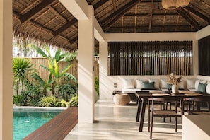 A modern interior with a pool, wooden deck, and a seating area with a sofa and table. - Nayma Villas (General Luna)