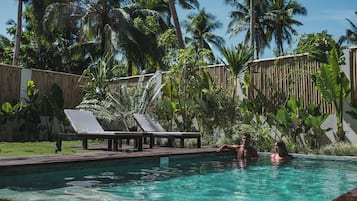 A swimming pool with lounge chairs, surrounded by tropical vegetation and a bamboo fence.