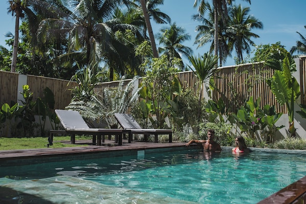 A swimming pool with lounge chairs, surrounded by tropical vegetation and a bamboo fence. - Nayma Villas (General Luna)