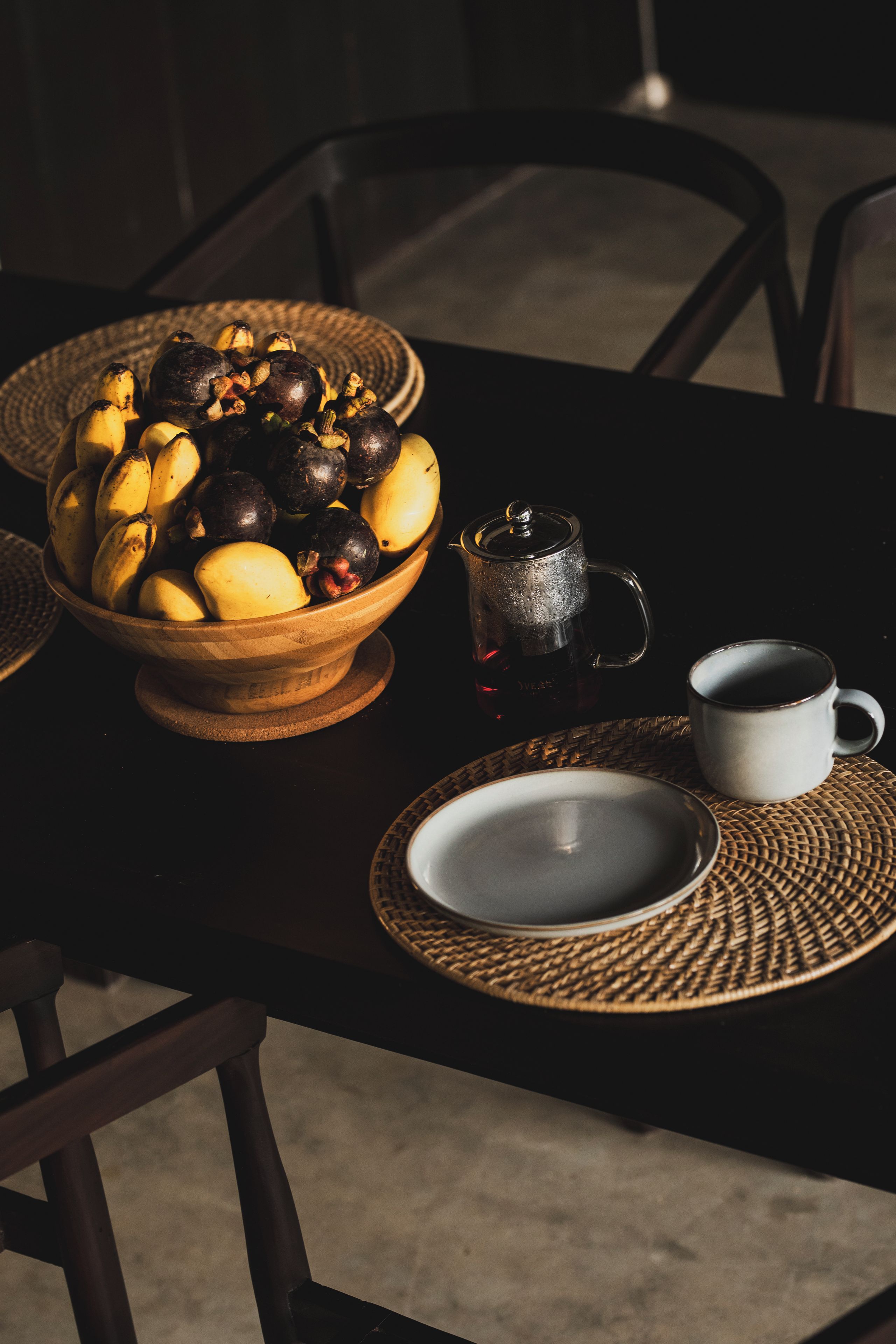 Een eettafel met een fruitschaal, een koffiepot en een kop.