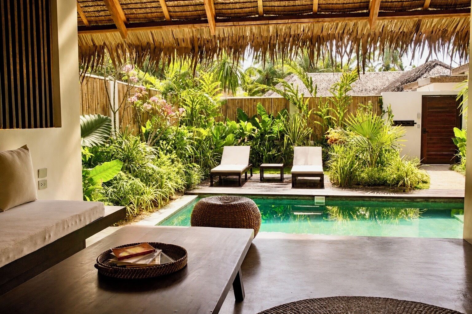 A poolside area with lounge chairs, a table, and a thatched roof structure.