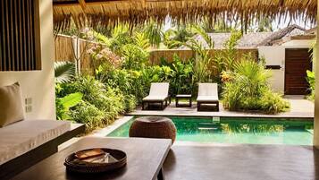 A poolside area with lounge chairs, a table, and a thatched roof structure.