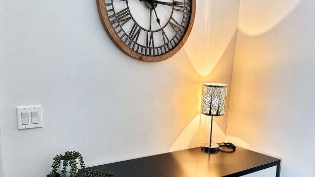 A modern desk with a wall-mounted clock, a lamp, and a small plant.