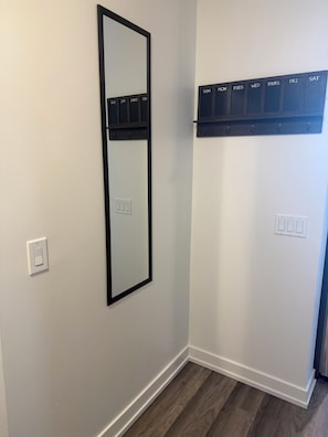 Une pièce avec un miroir fixé au mur, un interrupteur et un calendrier au-dessus d’une porte.