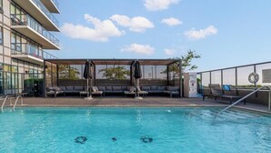 A swimming pool with a shallow area marked, lounge chairs, and a covered seating area.