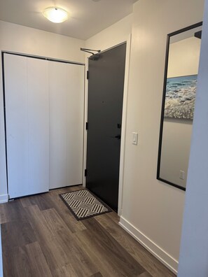 Un couloir avec une porte sombre, une armoire blanche et un miroir au mur.