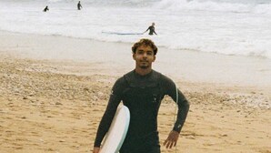 A person in a wetsuit holding a surfboard on a sandy beach with waves in the background.