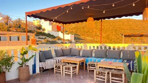 An outdoor seating area with a sofa, chairs, and a table, under a shaded canopy with string lights.